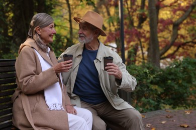 Photo of Affectionate senior couple with cups of coffee spending time together on bench in autumn park