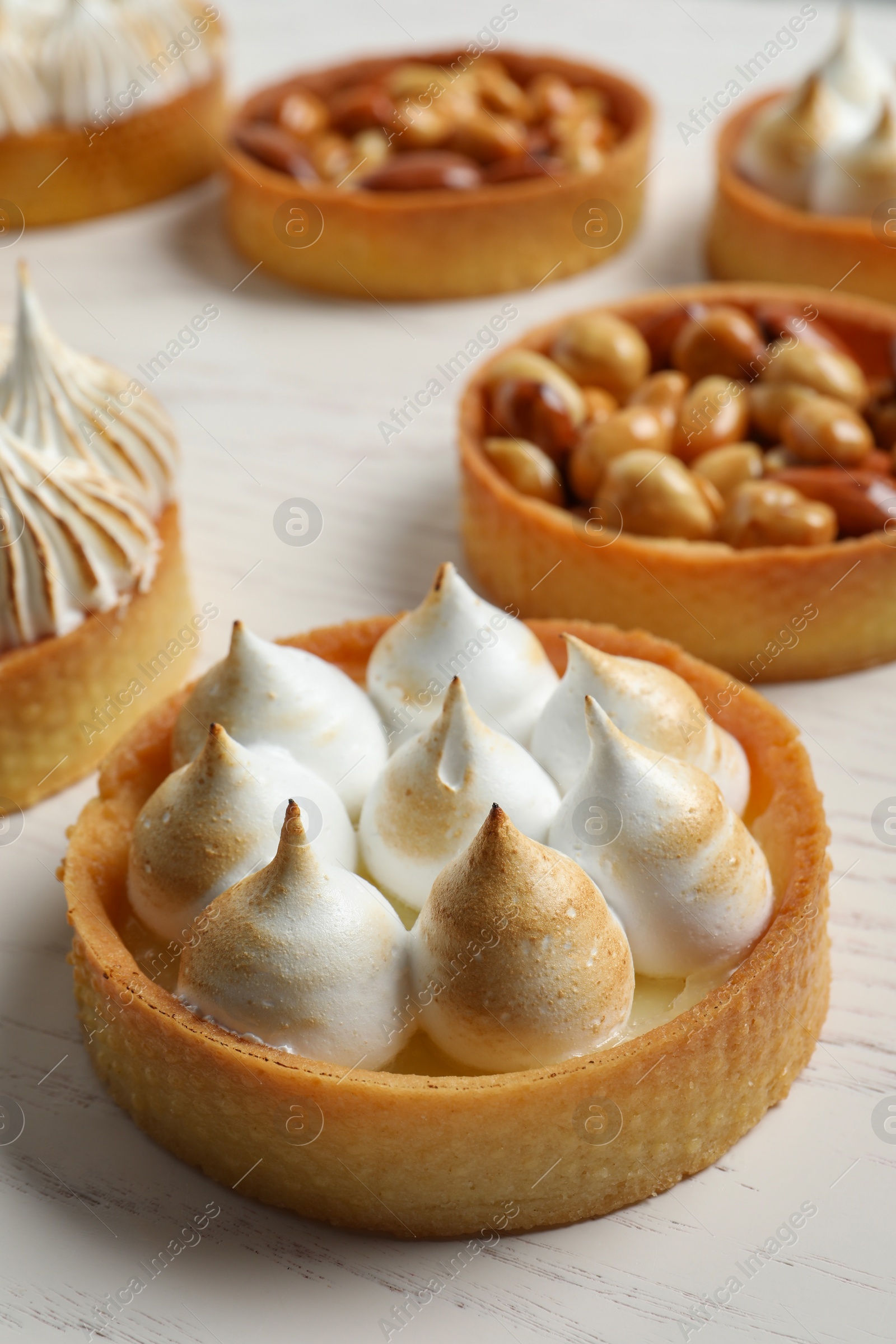Photo of Many different tartlets on white wooden table, closeup. Delicious dessert