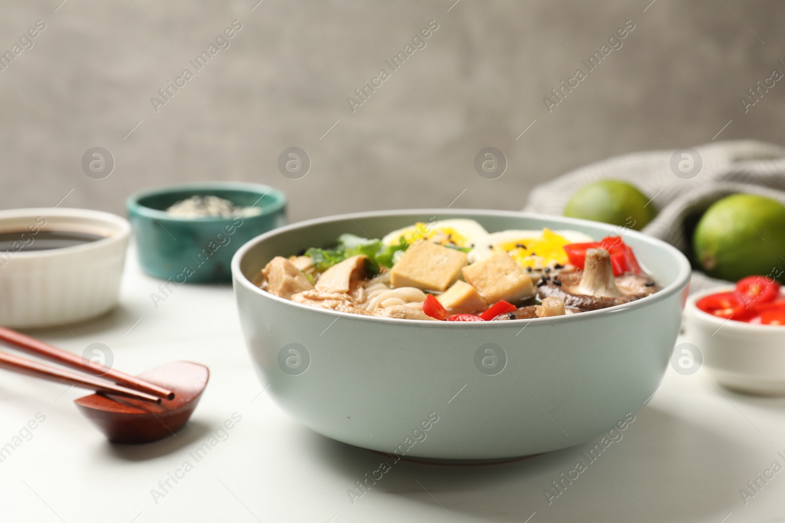 Photo of Bowl of delicious ramen, ingredients and chopsticks on white table, closeup. Noodle soup