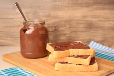 Photo of Tasty toasts with chocolate paste and jar of cream on beige table