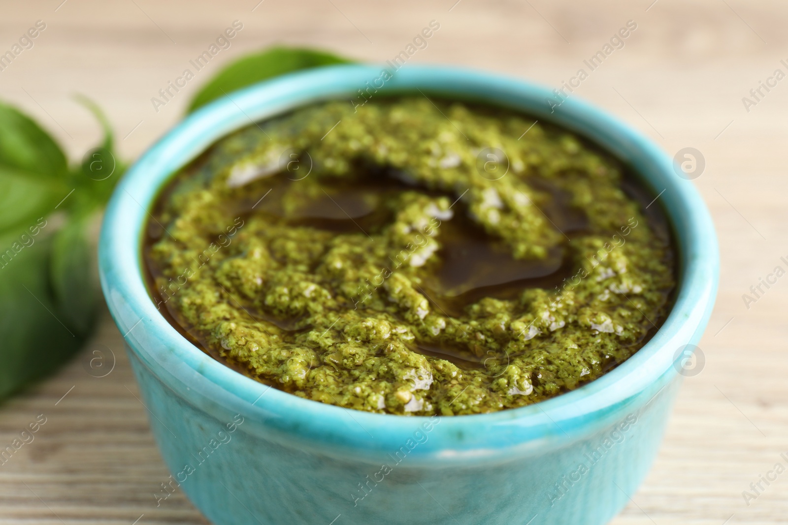 Photo of Tasty pesto sauce in bowl and basil on wooden table, closeup