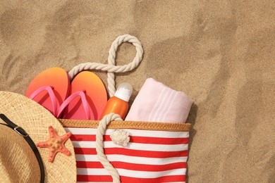 Photo of Stylish striped bag with beach accessories on sand, flat lay. Space for text