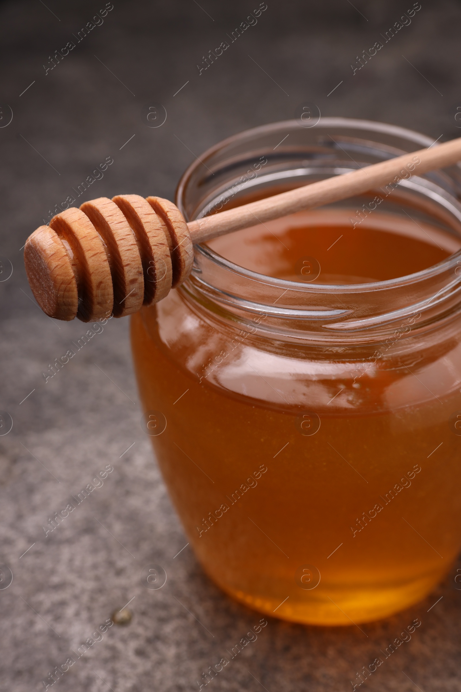 Photo of Sweet golden honey in jar and dipper on grey table, closeup