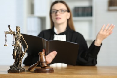 Judge with folder working in courtroom, selective focus. Mallet and figure of Lady Justice on wooden table