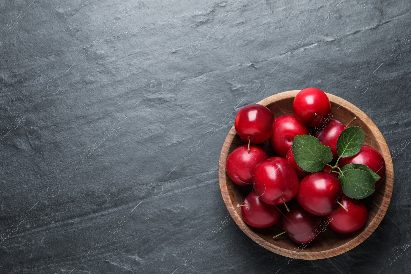 Photo of Delicious ripe cherry plums with leaves on black table, top view. Space for text