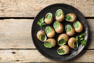 Delicious cooked snails with parsley on wooden table, top view. Space for text