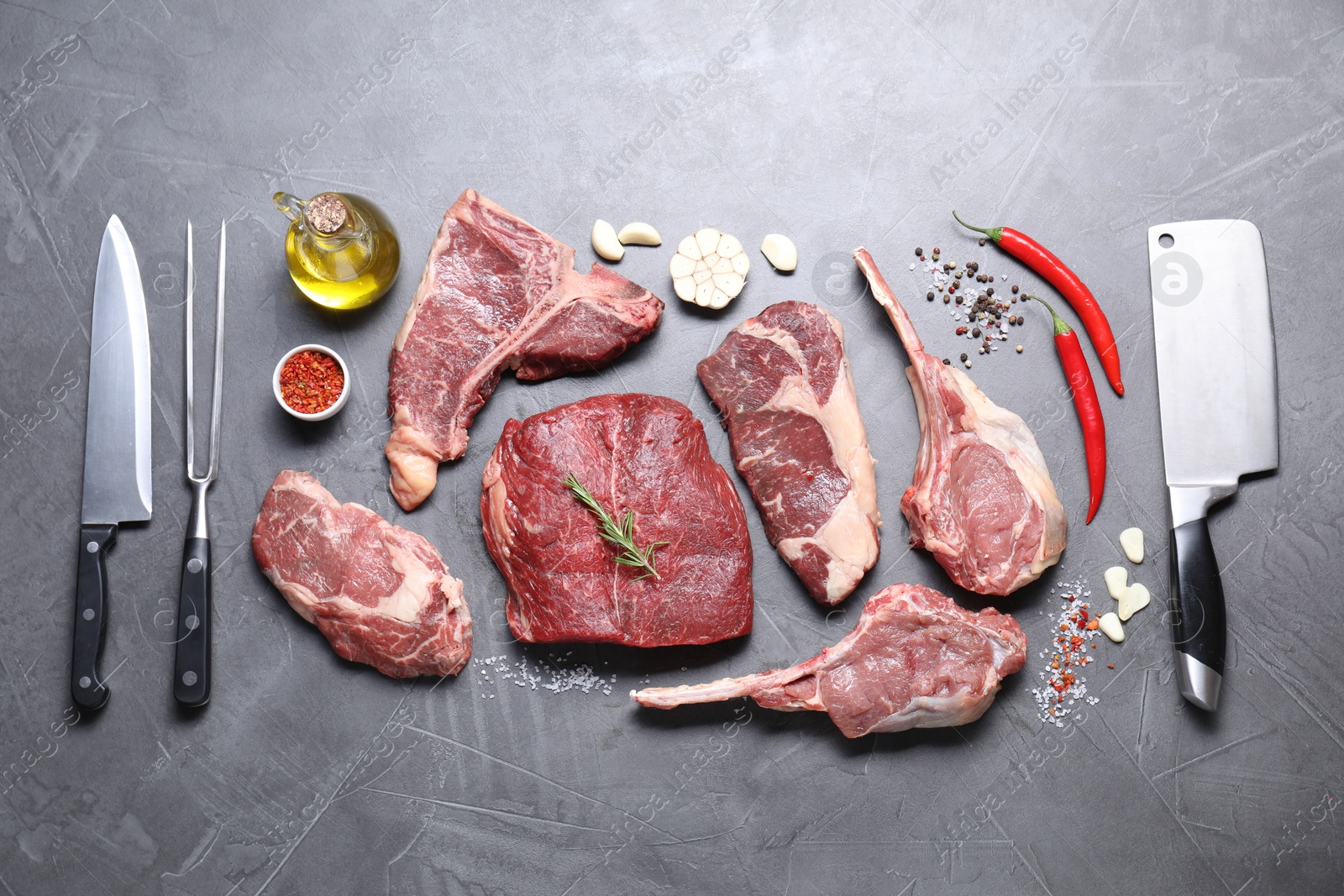 Photo of Fresh raw beef cuts, spices and butcher tools on light grey textured table, flat lay