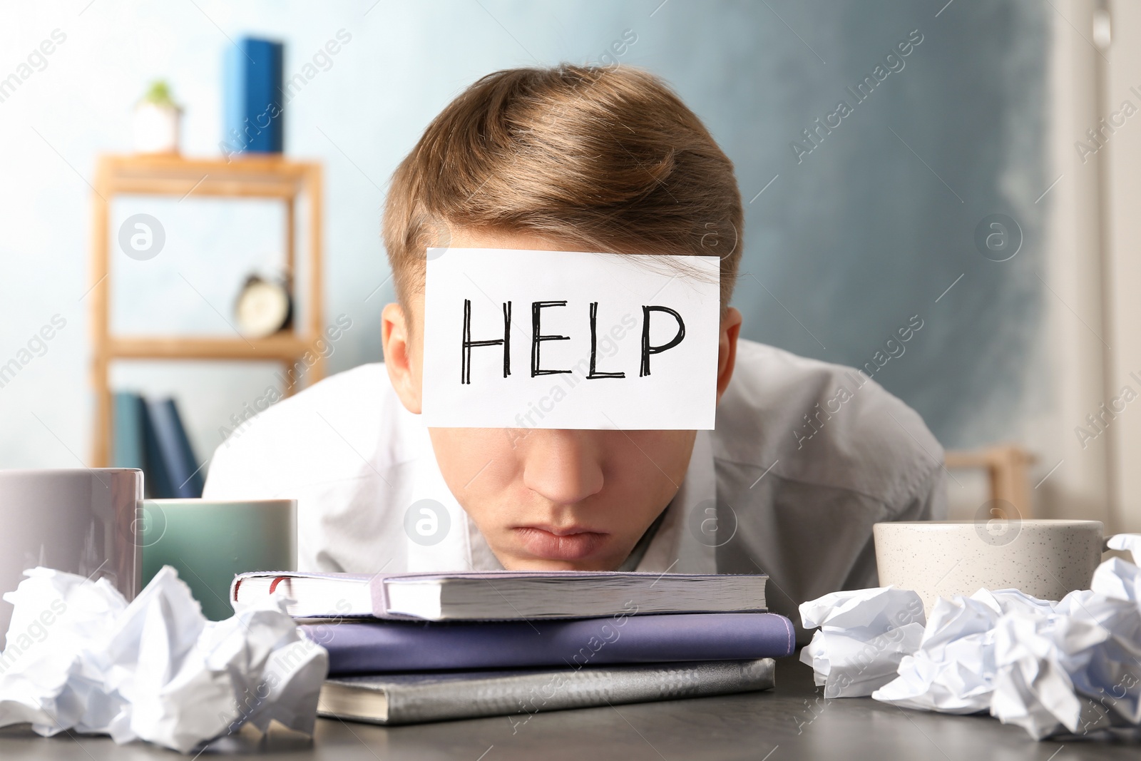 Photo of Young man with note HELP on forehead at workplace