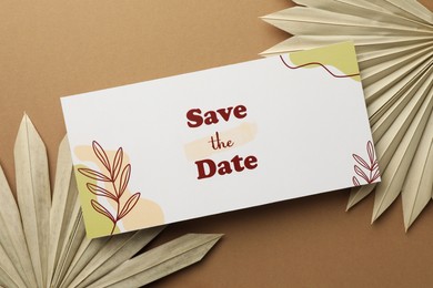 Beautiful card with Save the Date phrase and leaves on beige background, top view