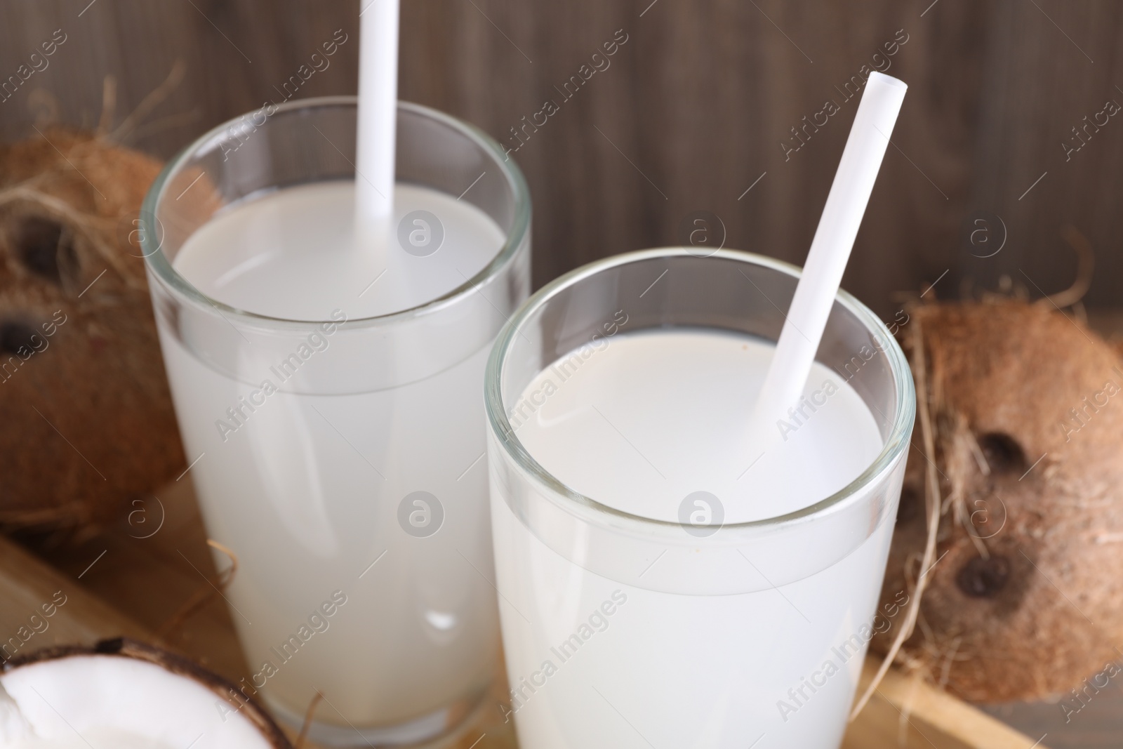 Photo of Glasses of coconut water with straws and nuts on table, closeup