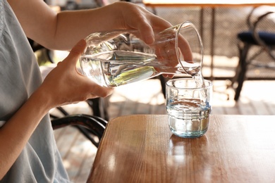 Photo of Woman pouring water into glass on wooden table indoors
