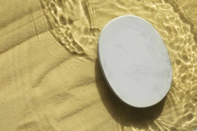 Photo of Stylish presentation for product. Stone podium in water on sand, top view. Space for text