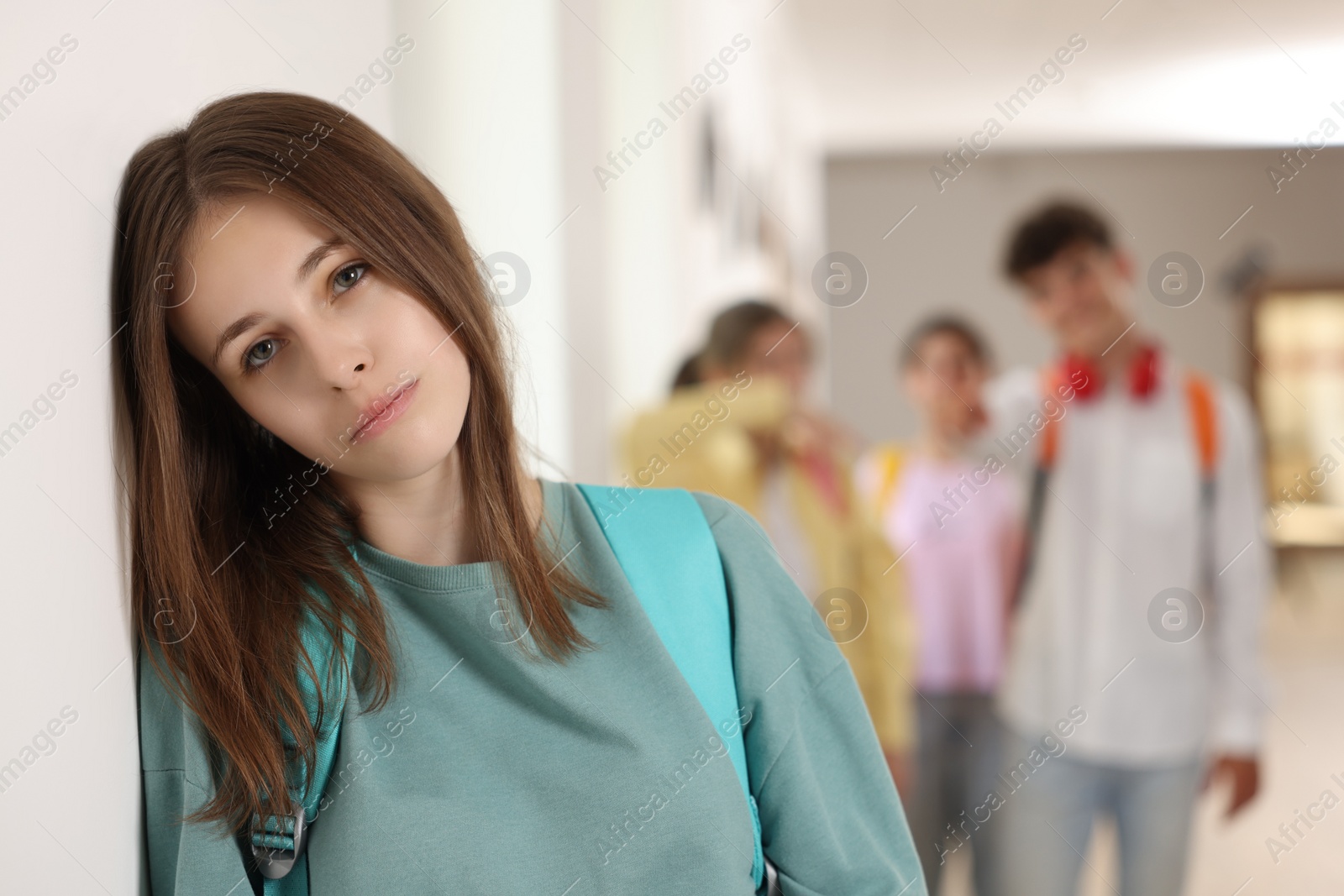 Photo of Teen problems. Lonely girl standing separately from other students at school