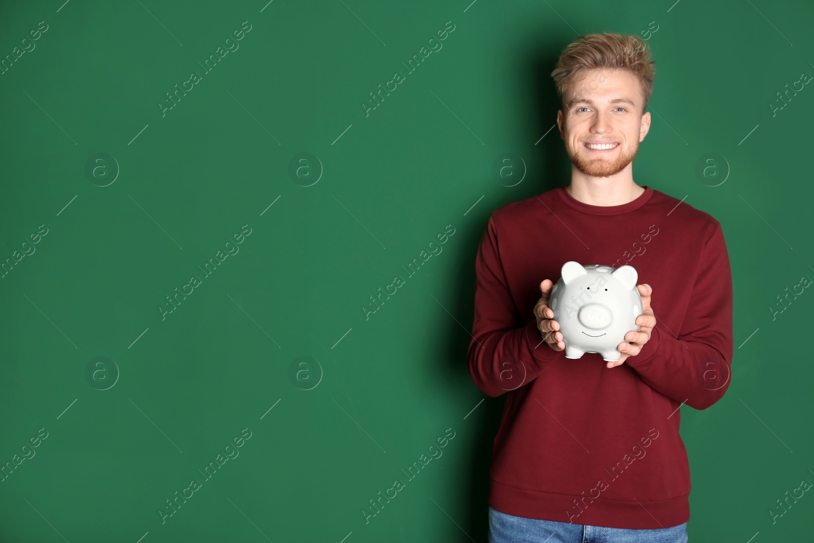 Photo of Young man with piggy bank on color background, space for text. Money saving