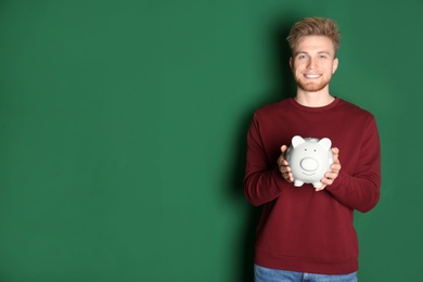 Young man with piggy bank on color background, space for text. Money saving