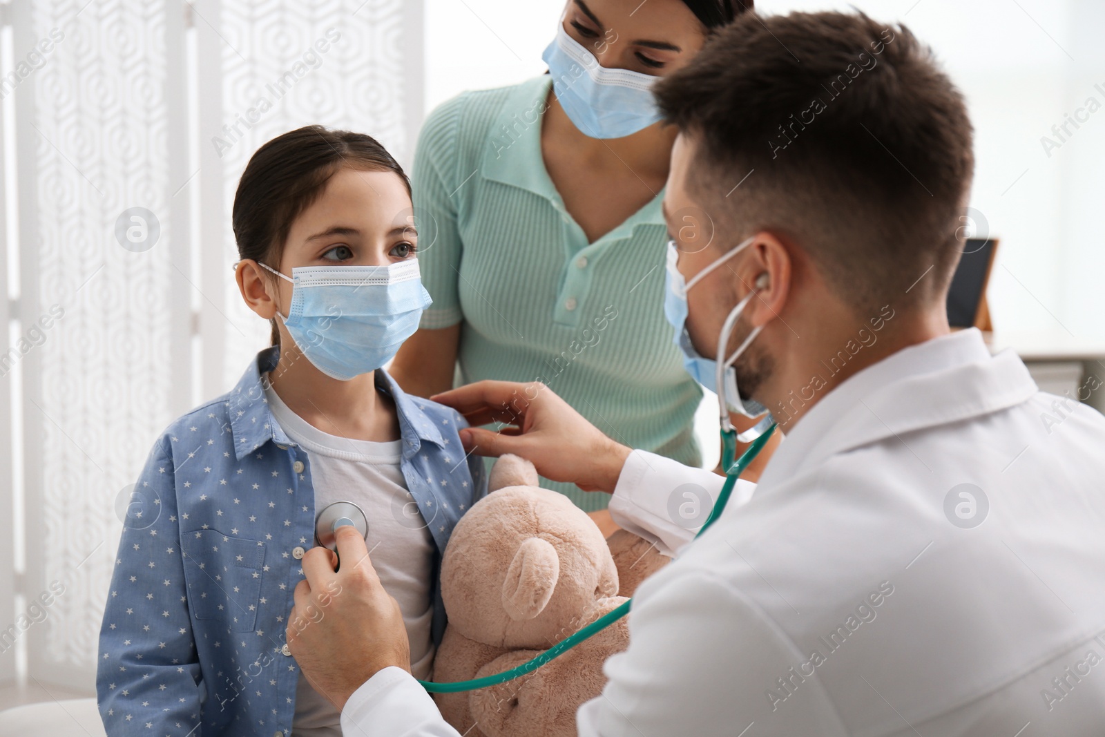 Photo of Mother with daughter visiting pediatrician in hospital. Wearing protective masks