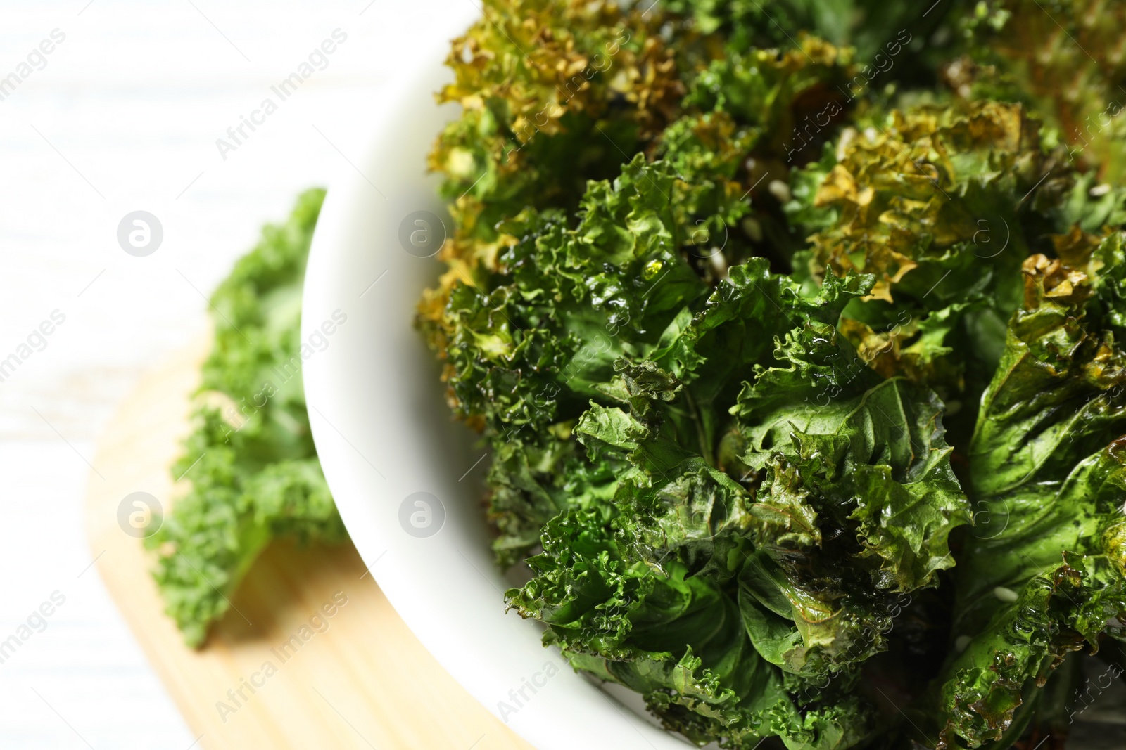 Photo of Tasty baked kale chips in bowl on table, closeup