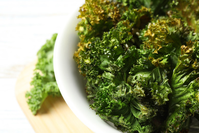 Photo of Tasty baked kale chips in bowl on table, closeup