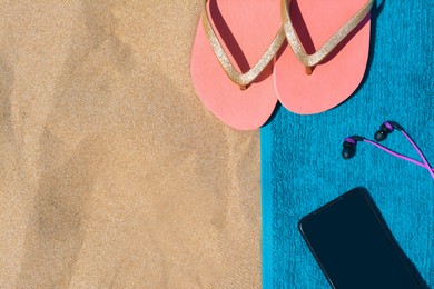 Photo of Soft blue beach towel with flip flops, smartphone and earphones on sand, flat lay. Space for text