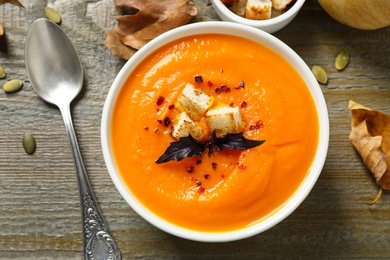 Photo of Delicious pumpkin soup in bowl on wooden table, flat lay