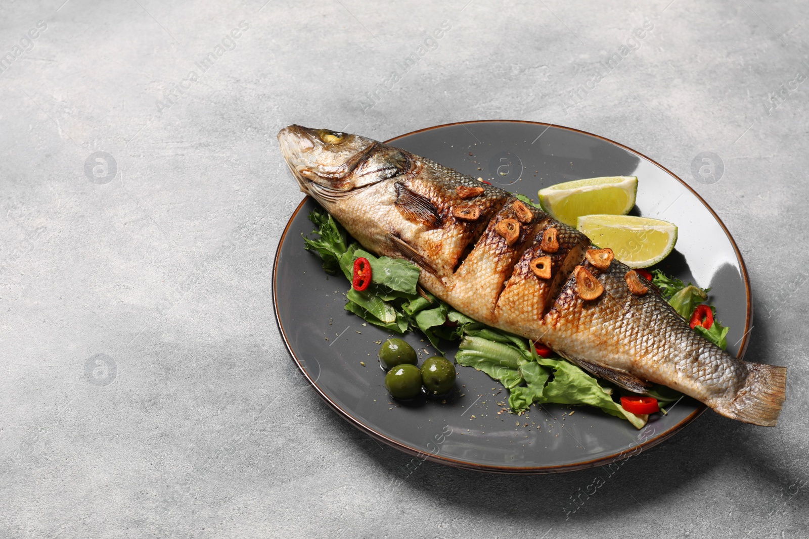 Photo of Plate with delicious sea bass fish and ingredients on light grey table, space for text