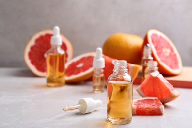 Photo of Bottles of essential oil and grapefruits on grey table, space for text