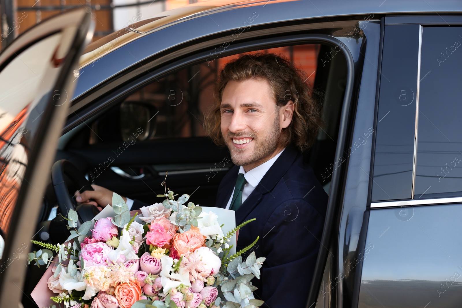 Photo of Young handsome man with beautiful flower bouquet in car