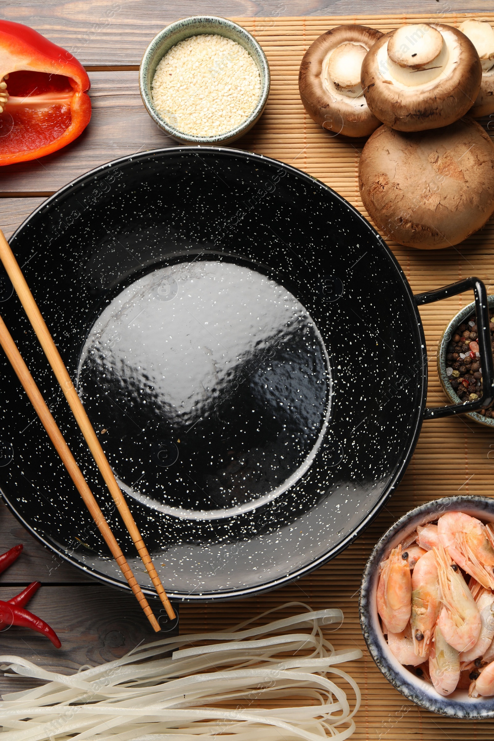 Photo of Black wok, chopsticks and products on color wooden table, flat lay