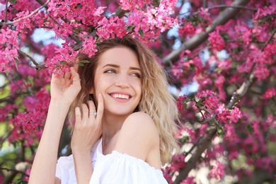 Photo of Attractive young woman posing near blossoming tree on sunny spring day