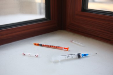 Photo of Disposable syringes with needles on white window sill