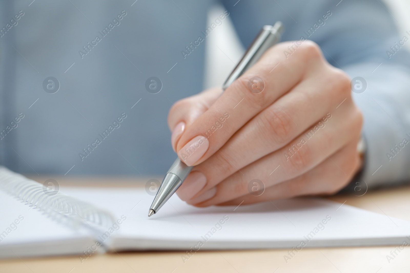 Photo of Woman writing in notebook at wooden table, closeup