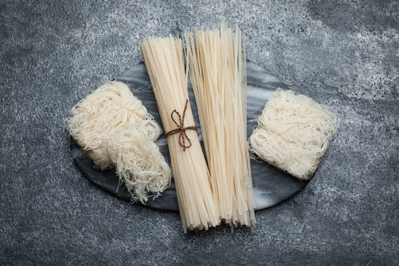 Photo of Different uncooked rice noodles on grey table, top view