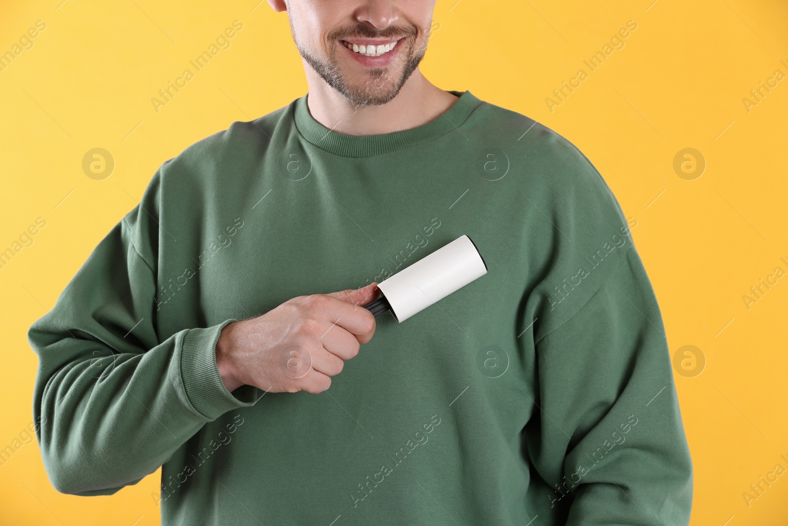 Photo of Man cleaning clothes with lint roller on yellow background, closeup