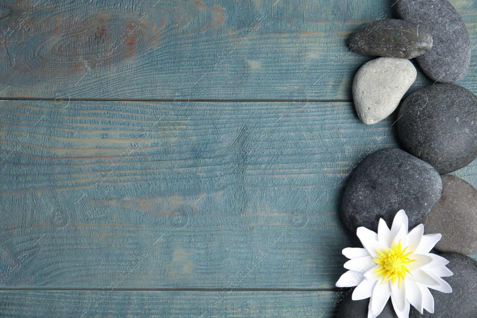 Photo of Stones with lotus flower and space for text on blue wooden background, flat lay. Zen lifestyle