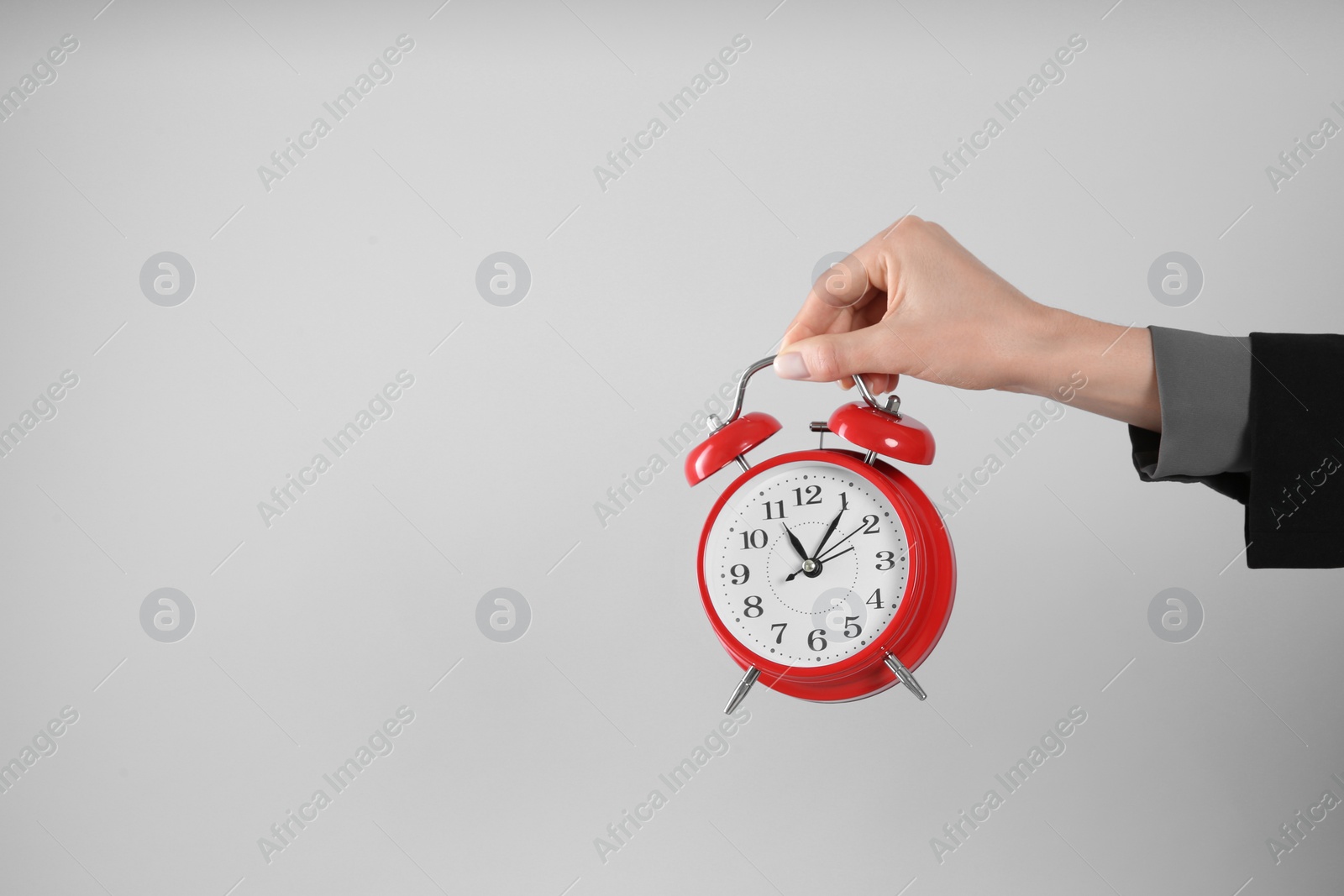 Photo of Businesswoman holding alarm clock on light grey background, closeup with space for text. Time management