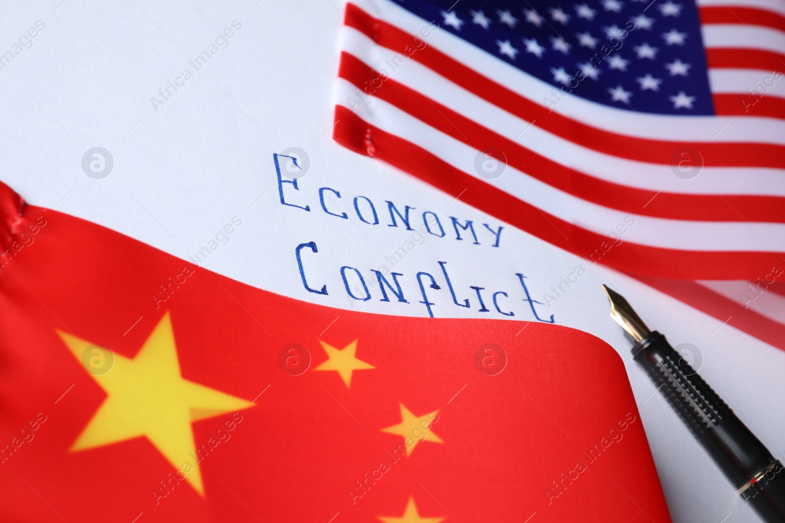 Photo of USA and China flags, pen on paper with text ECONOMY CONFLICT, closeup