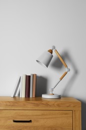 Photo of Stylish lamp and books on wooden table near white wall. Interior design