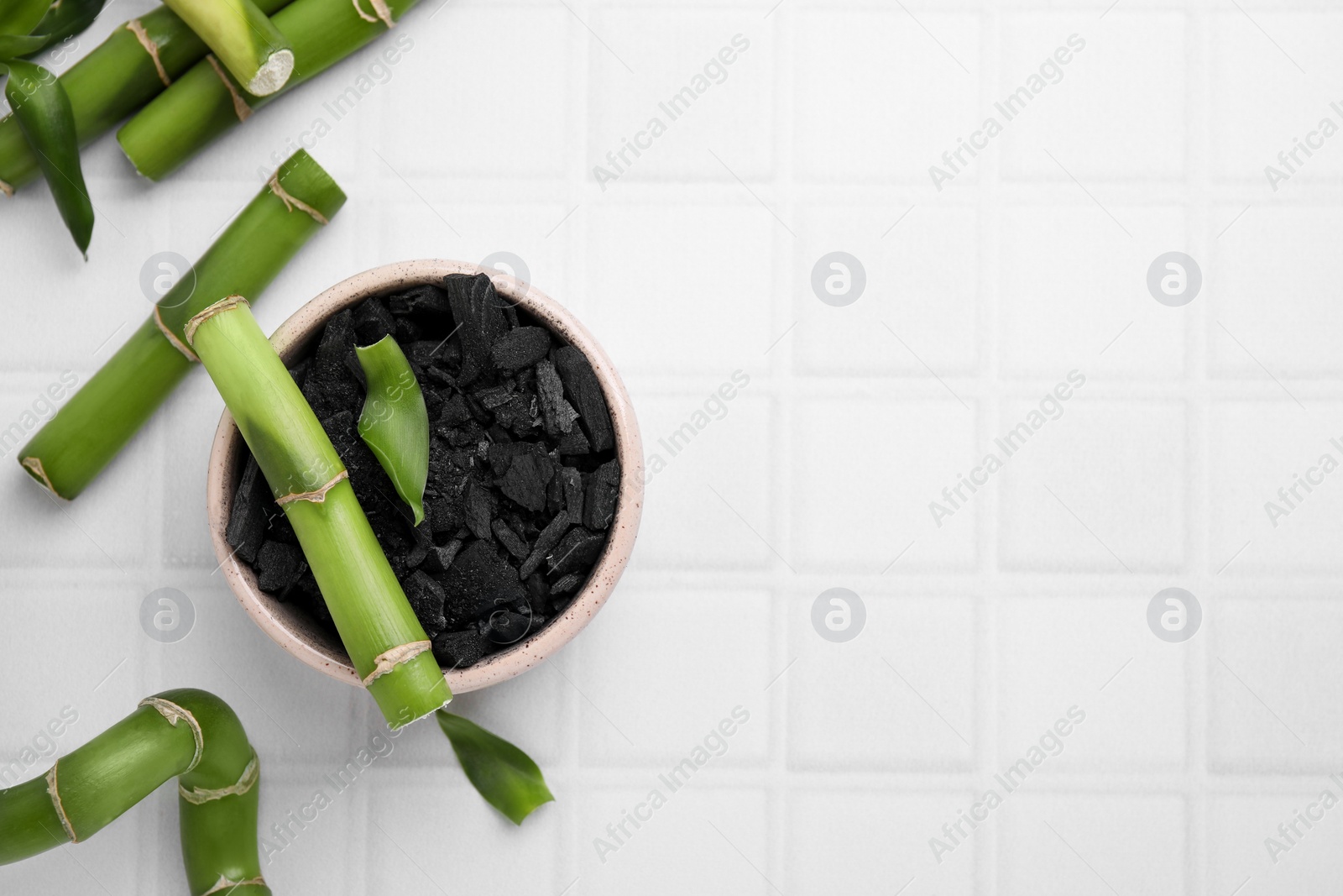 Photo of Fresh bamboo and charcoal on white tiled table, flat lay. Space for text