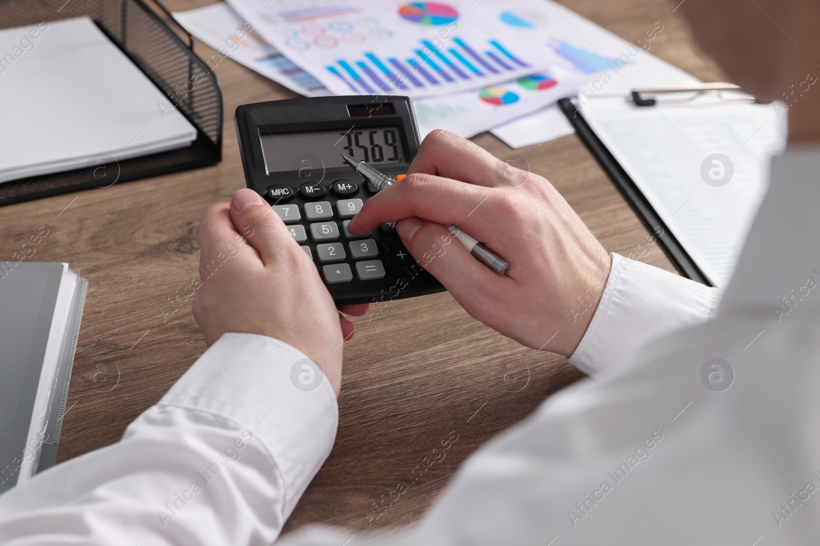 Photo of Man using calculator at wooden table, closeup