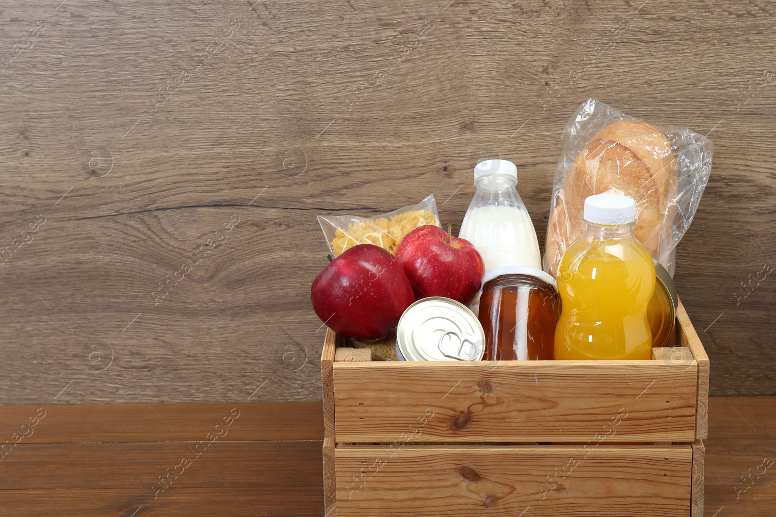 Photo of Humanitarian aid. Different food products for donation in crate on wooden table. Space for text