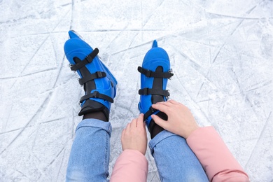 Photo of Woman adjusting figure skate while sitting on ice rink, closeup