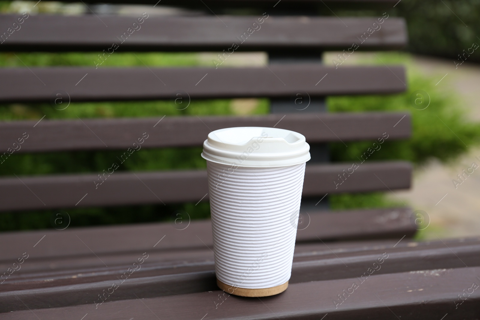 Photo of Paper cup of coffee on wooden bench outdoors. Takeaway drink