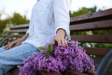 Photo of Young woman with lilac flowers on wooden bench outdoors