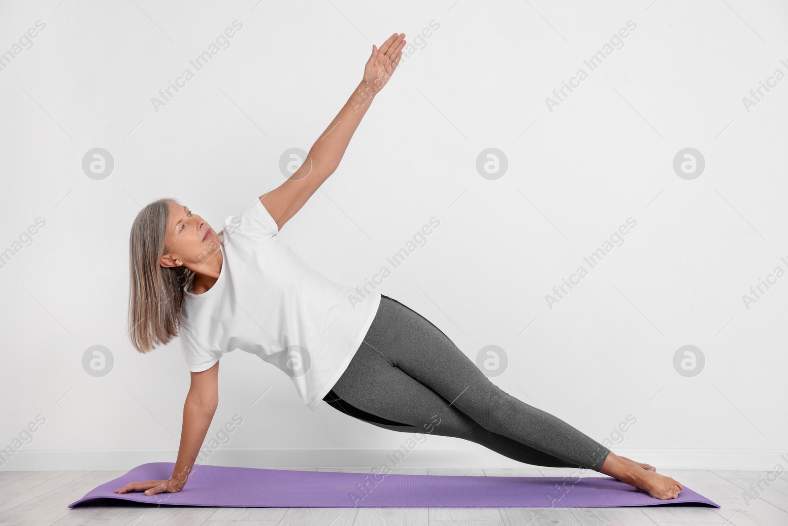 Photo of Senior woman practicing yoga on mat near white wall