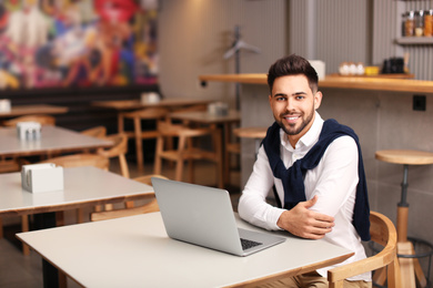 Photo of Young male business owner working with laptop in his cafe. Space for text