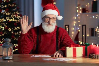 Photo of Santa Claus waving hello at his workplace in room decorated for Christmas