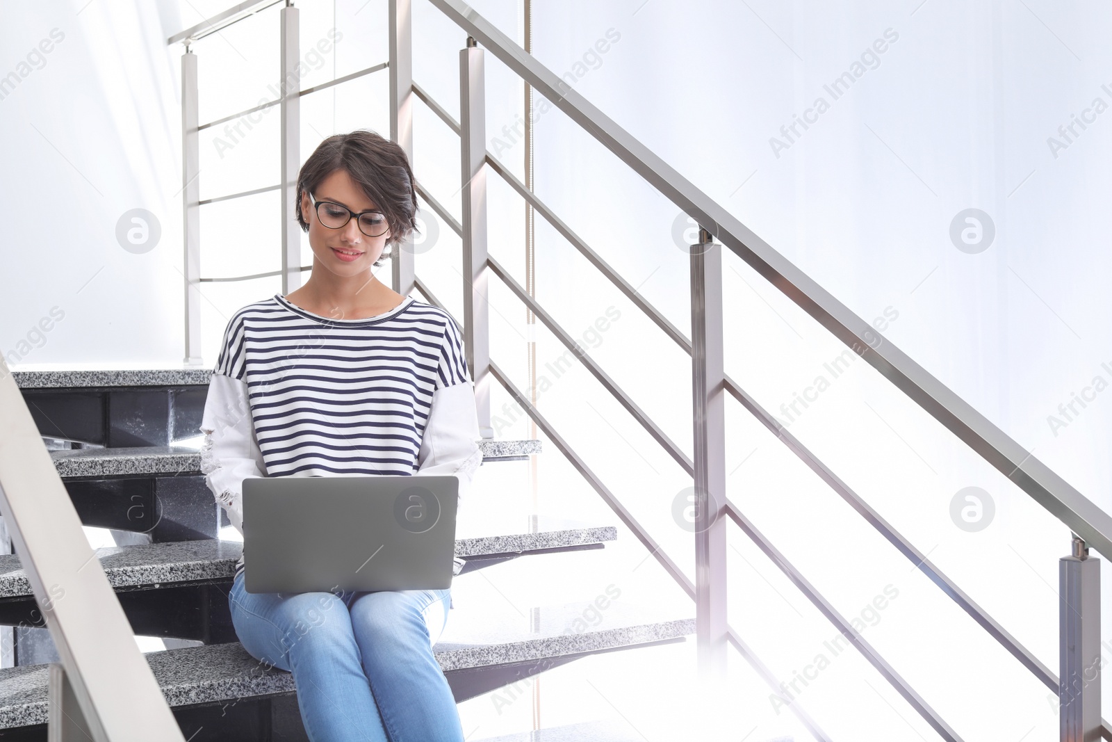 Photo of Young woman with modern laptop sitting on stairs indoors