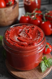 Photo of Jar of tasty tomato paste and ingredients on grey textured table, closeup