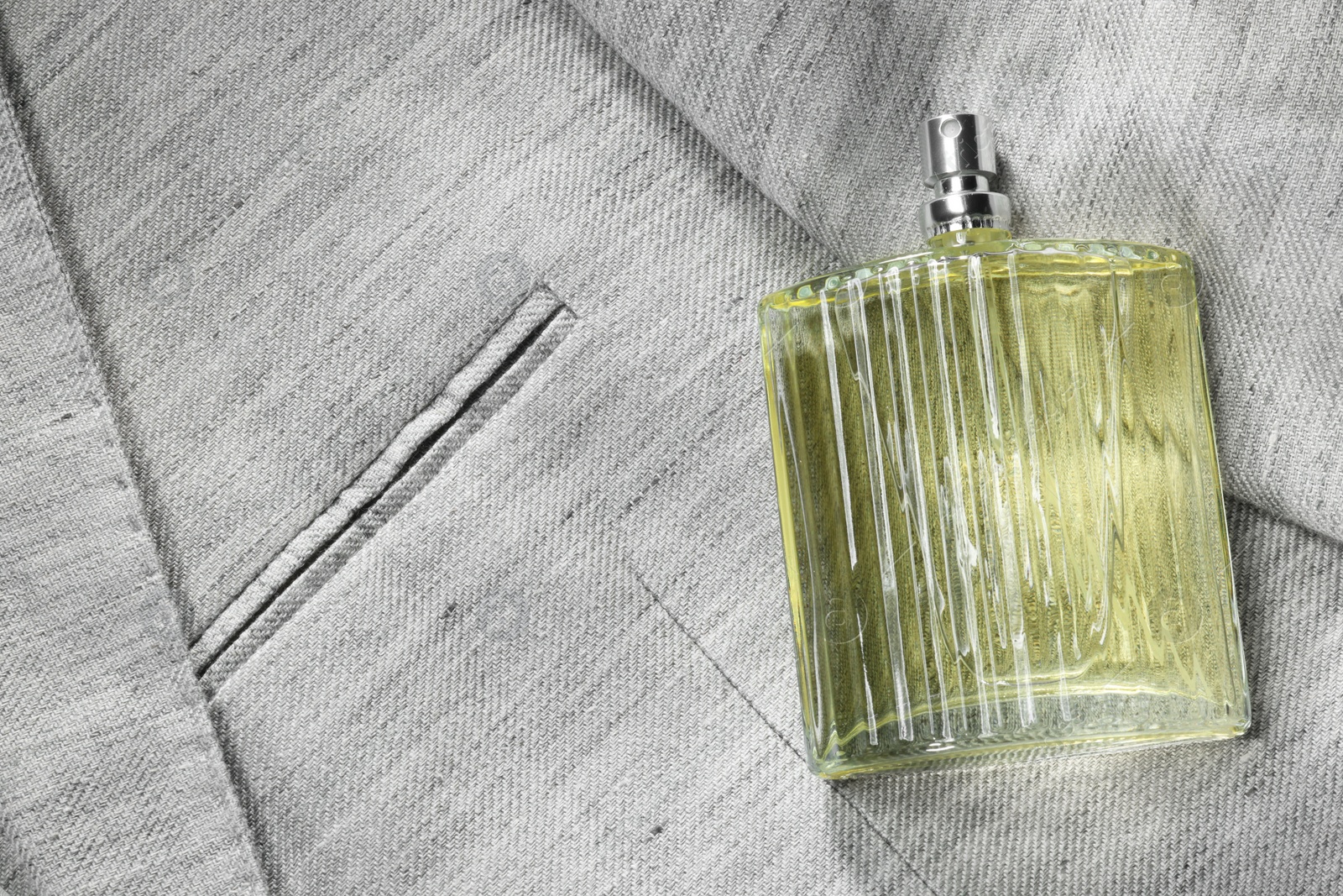 Photo of Luxury men's perfume in bottle on grey jacket, top view. Space for text