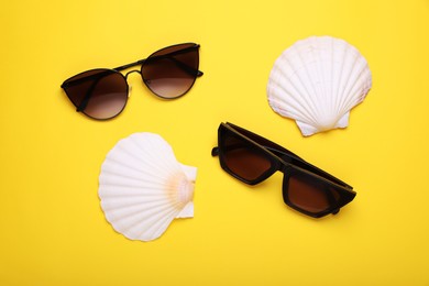 Photo of Stylish sunglasses and seashells on yellow background, flat lay